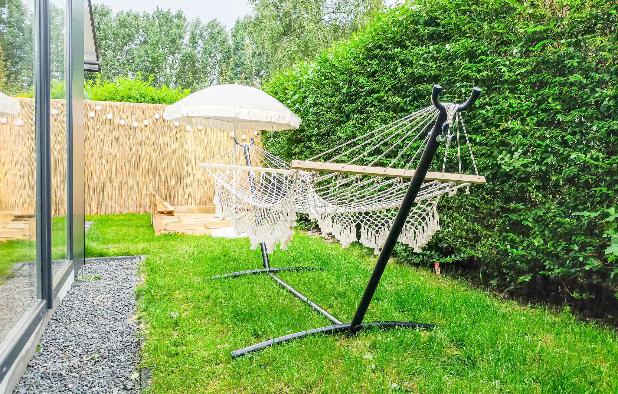 A hammock chair with a canopy, a wooden deck, and a hedge in a garden setting.