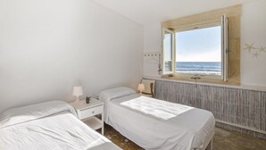 A bedroom with two beds, a window with a view of the sea, a radiator, and a small bedside table with a lamp. - 3 bedroom beach front home in Siracusa (Siracusa)