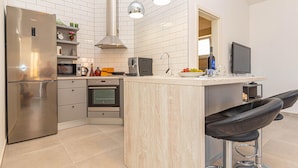 Una cocina moderna con un refrigerador de acero inoxidable, horno empotrado, microondas y cafetera. Hay una isla de madera con taburetes de bar y un ventanal sobre el fregadero.