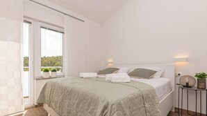 Un dormitorio moderno con una cama grande, una mesita de noche con lámpara y vistas a zonas verdes por la ventana.
