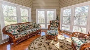 A sunroom with a large, floral-patterned sofa and armchairs, wooden flooring, and large windows offering a view of the outdoors. - Fantastic for a small family or multiple families! 
Also check vrbo.com/3702514 (Banner Elk)