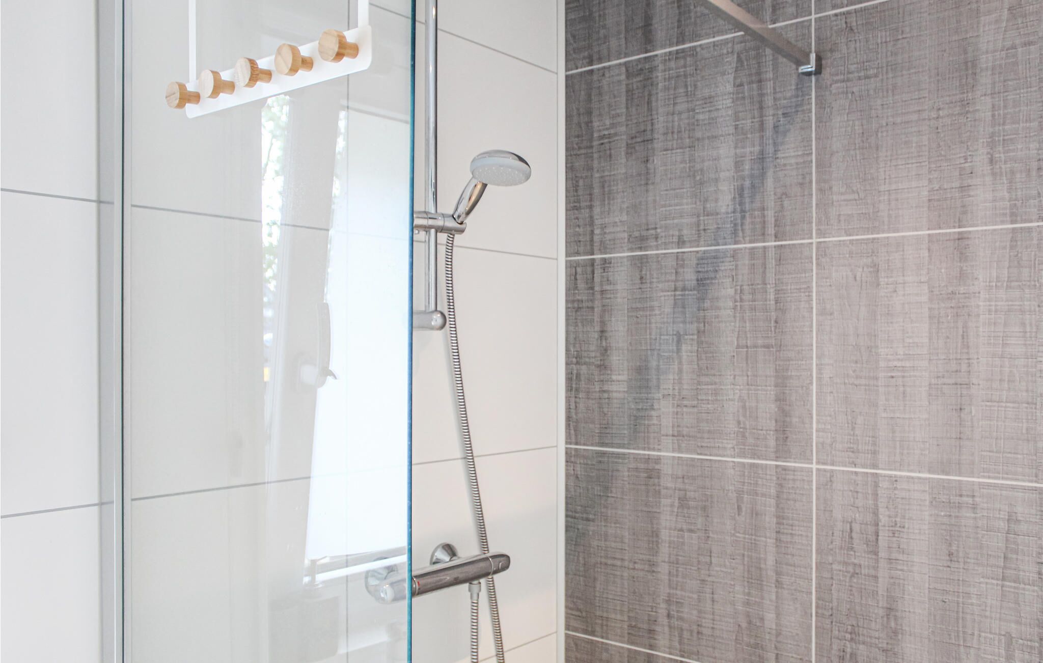 A shower area with a glass door, a handheld showerhead, and a wall-mounted faucet.