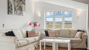 A living room with a beige sofa, a white coffee table, and a large window with a view of a field. - Nice home in Søllested with sauna (Søllested)