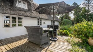 A thatched-roof house with a wooden deck, wicker furniture, and a grill. - Nice home in Søllested with sauna (Søllested)