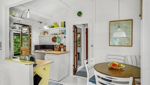 A compact kitchen with a stove, sink, and various utensils. There's a dining area with a table and chairs, and a window with a view of greenery. - Cozy home in Jægerspris with WiFi (Jægerspris)