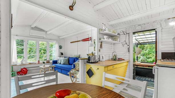 A bright, open-plan living and kitchen area with a blue sofa, wooden dining table, and a fruit bowl. - Cozy home in Jægerspris with WiFi (Jægerspris)