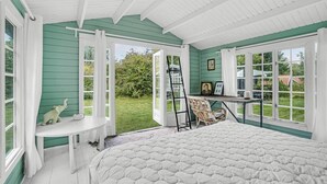 A bedroom with a large bed, a desk, and a chair. There are two windows and a door leading to a garden. - Cozy home in Jægerspris with WiFi (Jægerspris)