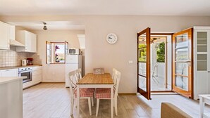A kitchen with a dining table, chairs, a clock, and a view through an open door. - Cozy apartment in Zaboric with kitchen (Zaboric)