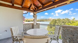 A covered outdoor seating area with a table and chairs, overlooking a body of water and greenery. - Cozy apartment in Zaboric with kitchen (Zaboric)