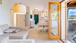 A modern living room with a sofa and a dining area with chairs and a table. There is a kitchen visible in the background with cabinets and a stove. - Cozy apartment in Zaboric with kitchen (Zaboric)