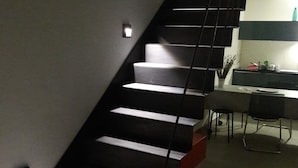 A modern staircase with a black railing leading to a kitchen area.