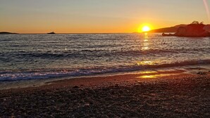 A sunset over a rocky beach with waves gently lapping at the shore.