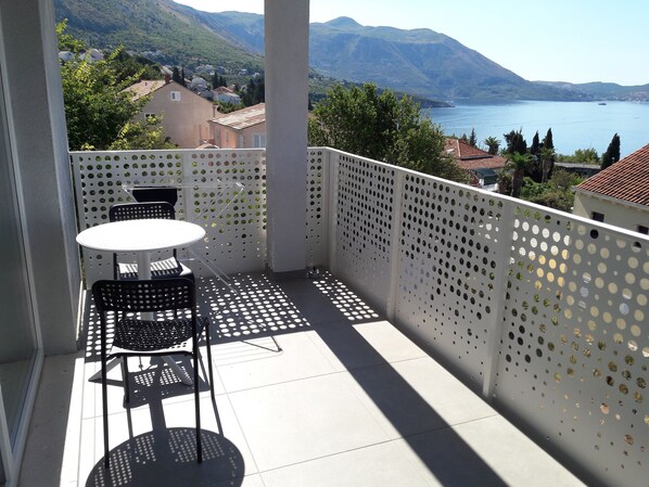 A balcony with a table and chairs, overlooking a lake and mountains.