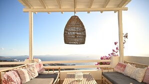 A balcony with a wicker hanging light fixture, cushioned seating, and a table with a glass vase. - Villa Santa Andrea with a fantastic 180 degree sea view (Mykonos)