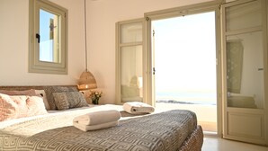 A bedroom with a bed, pillows, a bedside table, a hanging light, and a view of the beach through an open door. - Villa Santa Andrea with a fantastic 180 degree sea view (Mykonos)