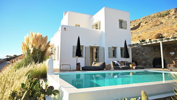 A modern white building with a pool, outdoor seating, and a stone wall. - Villa Santa Andrea with a fantastic 180 degree sea view (Mykonos)