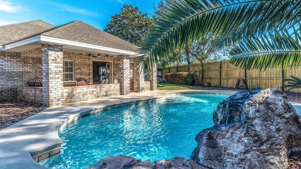 A pool area with a stone house, a wooden fence, and a palm tree. - Minutes from Destin Beaches (Fort Walton Beach)