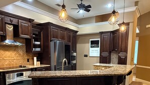 A modern kitchen with dark wood cabinets, stainless steel appliances, a granite countertop, and a central island with bar stools. - Minutes from Destin Beaches (Fort Walton Beach)
