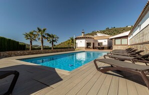 A swimming pool with lounge chairs, a stone wall, and a view of a hill with trees. - Awesome home in Malaga (Malaga)