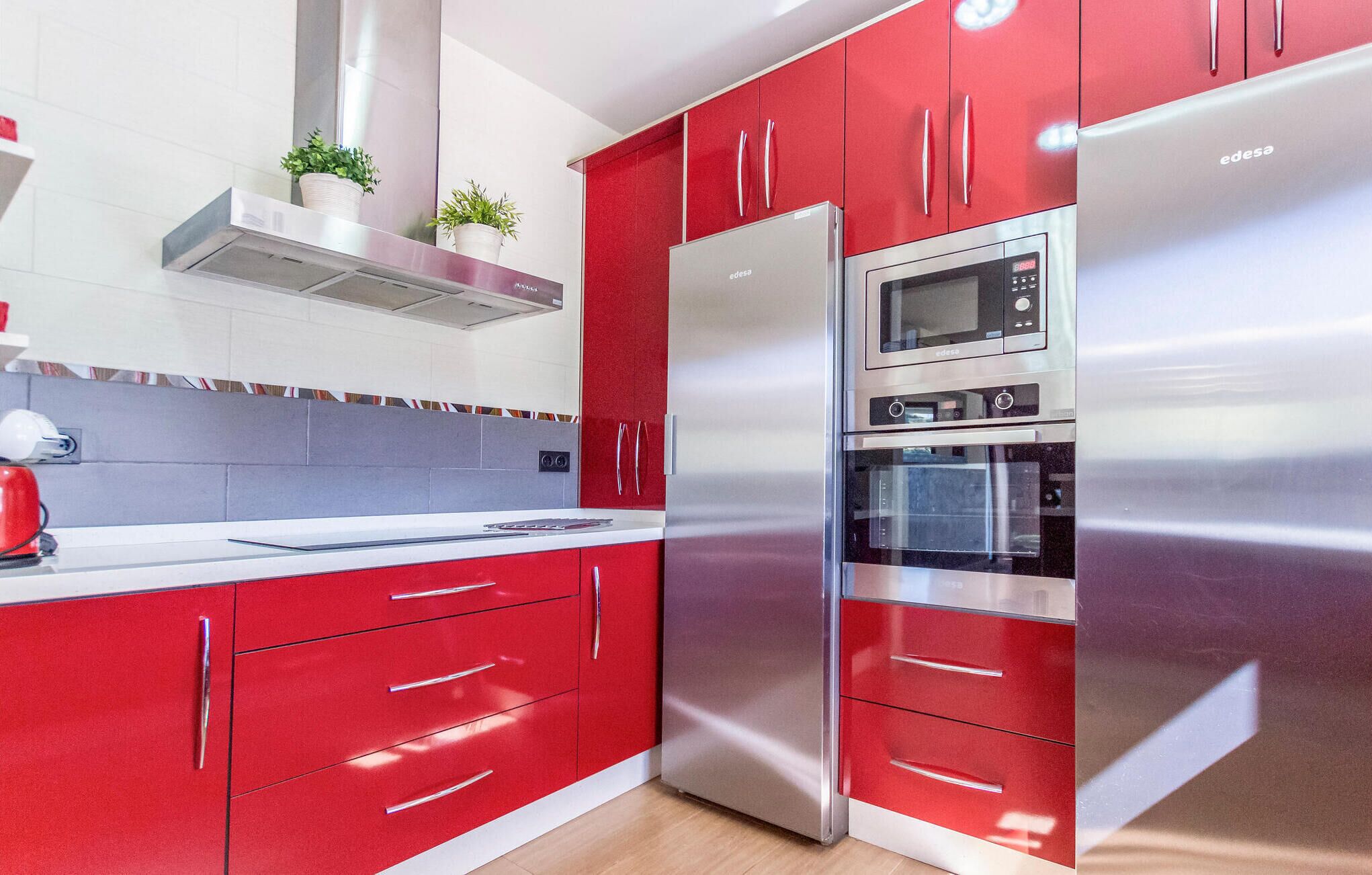 A modern kitchen with red cabinets, stainless steel appliances, and a microwave.