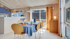 A dining area with a table set for four, surrounded by wooden chairs. A kitchen with blue cabinets is visible to the left.