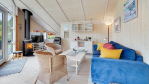 A cozy cabin interior with a fireplace, wicker furniture, a blue sofa, and a glass dining table.
