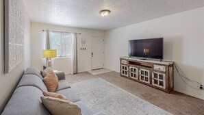 Un salon avec un canapé gris, un meuble TV en bois et une lampe.