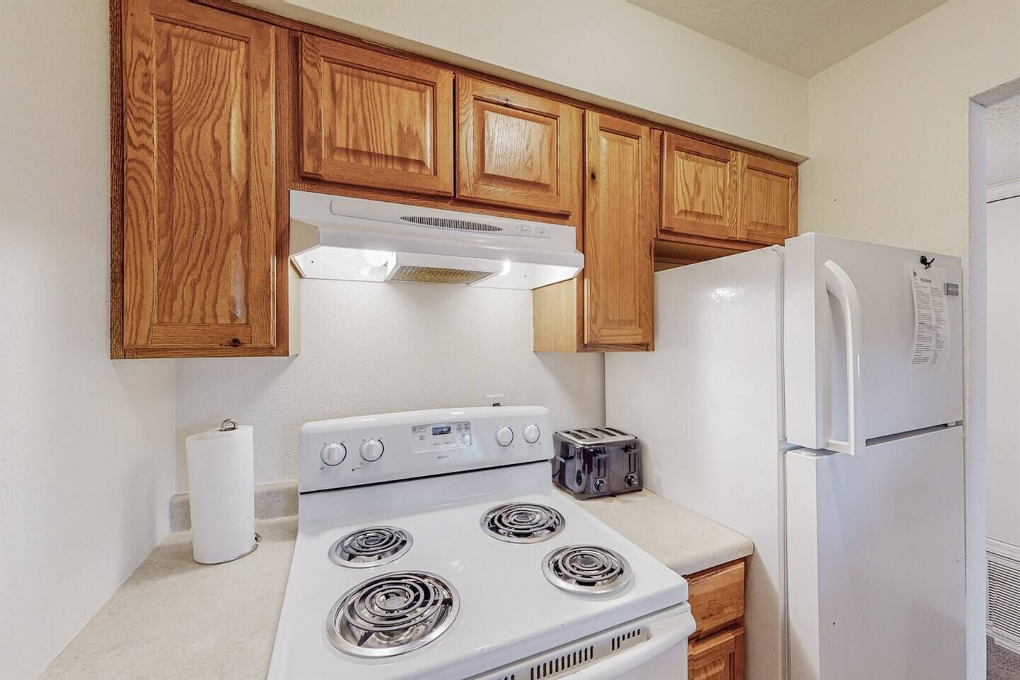 A kitchen with wooden cabinets, a white stove, a toaster, and a refrigerator.