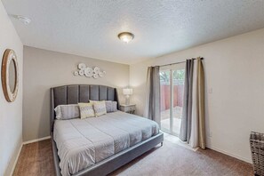 Une chambre avec un grand lit, une table de chevet, un luminaire fixé au mur et une porte-fenêtre coulissante donnant sur une terrasse.