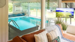 Una sala de estar moderna con un amplio ventanal con vistas a una piscina y un paisaje pintoresco.