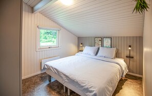 A bedroom with a sloped ceiling, a large bed, a window with a view of greenery, and two wall-mounted lamps. - Awesome home in Bindslev with sauna (Bindslev)