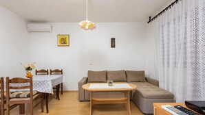 Un salon comprenant un canapé, une table à manger avec des chaises, une petite table avec un vase et un meuble pour la télévision avec une télécommande.