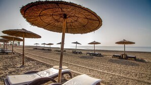 Uma praia com fileiras de espreguiçadeiras e toldos de palha.