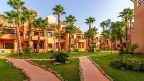 Um resort com vários edifícios, palmeiras e um jardim bem cuidado com caminhos.