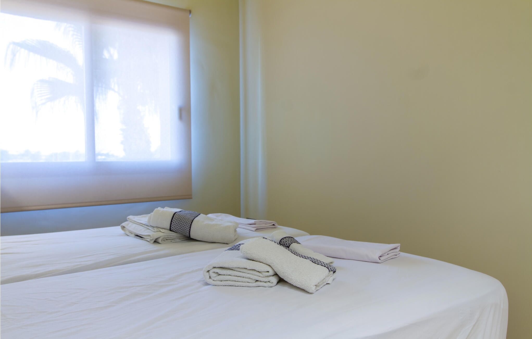 A hotel room with two beds, each with neatly folded white towels and a window with blinds.
