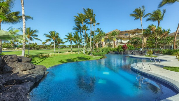 A swimming pool with clear blue water, surrounded by palm trees and a well-maintained lawn. - Beautifully decorated Penthouse overlooking WAIKOLOA Beach golf course (Waikoloa Village)