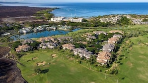 An aerial view of a coastal resort with multiple buildings, a golf course, and a body of water. - Beautifully decorated Penthouse overlooking WAIKOLOA Beach golf course (Waikoloa Village)