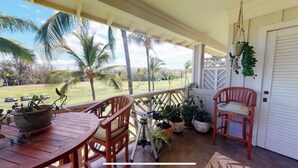 A covered porch with a wooden table and chairs, potted plants, and a view of a golf course. - Beautifully decorated Penthouse overlooking WAIKOLOA Beach golf course (Waikoloa Village)