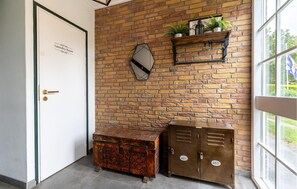 A room with a brick wall, a door labeled 'Laundry Room,' a mirror, a shelf with plants, and two metal storage units. - Cozy apartment in Zoutelande with WiFi (Zoutelande)