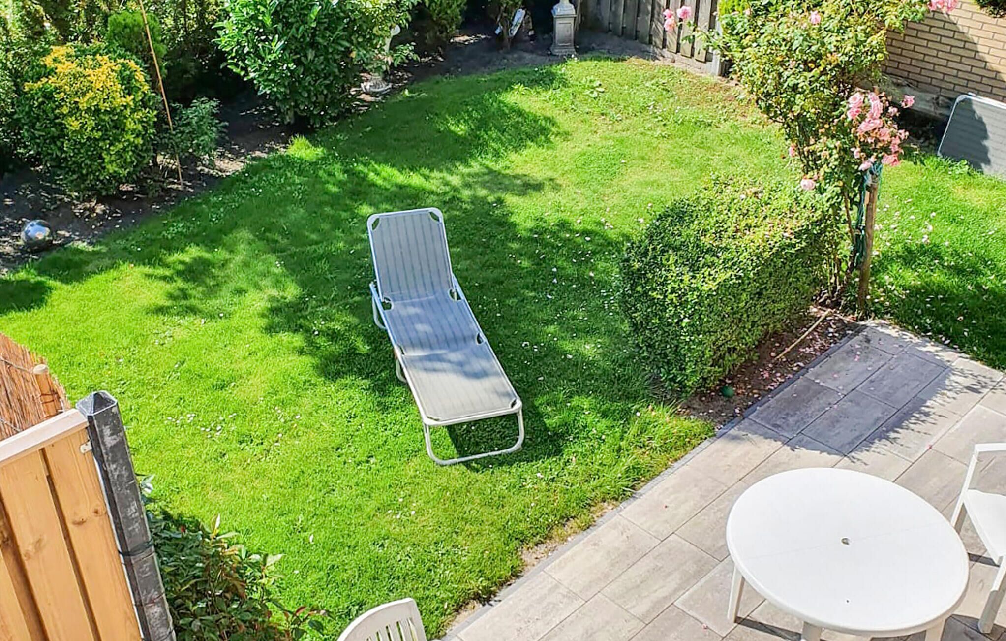 Un patio trasero con césped, una silla de metal, una mesa blanca y una valla de madera.
