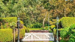 Un jardí amb tanca blanca, setges verdes i dos fanals.
