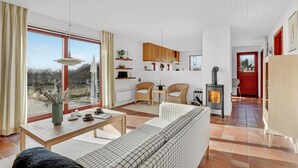A modern living room with a sofa, dining table, and chairs. There is a fireplace and a red door. - Beautiful home in Aakirkeby with WiFi (Aakirkeby)