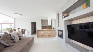 A modern living room with a large flat-screen TV, a built-in fireplace, and a kitchen area with bar stools. - Gorgeous home in Klis (Klis)