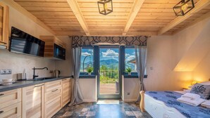 Un dormitorio pequeño con cama, una kitchenette y vistas a montañas a través de una puerta.