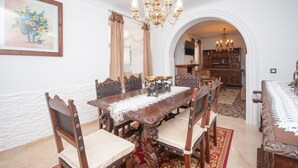 Un comedor con una mesa de madera, sillas y una araña. Se ve una cocina a través de un arco en el fondo.