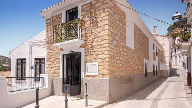 Un edificio de piedra con un balcón, una puerta y un letrero en la pared.