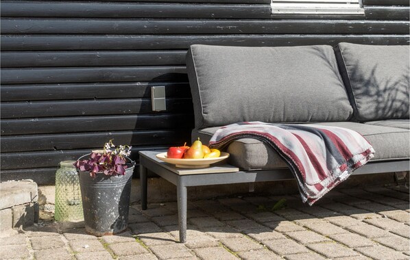 A black wooden wall, a grey sofa with a blanket, a small table with a fruit bowl, and a potted plant.