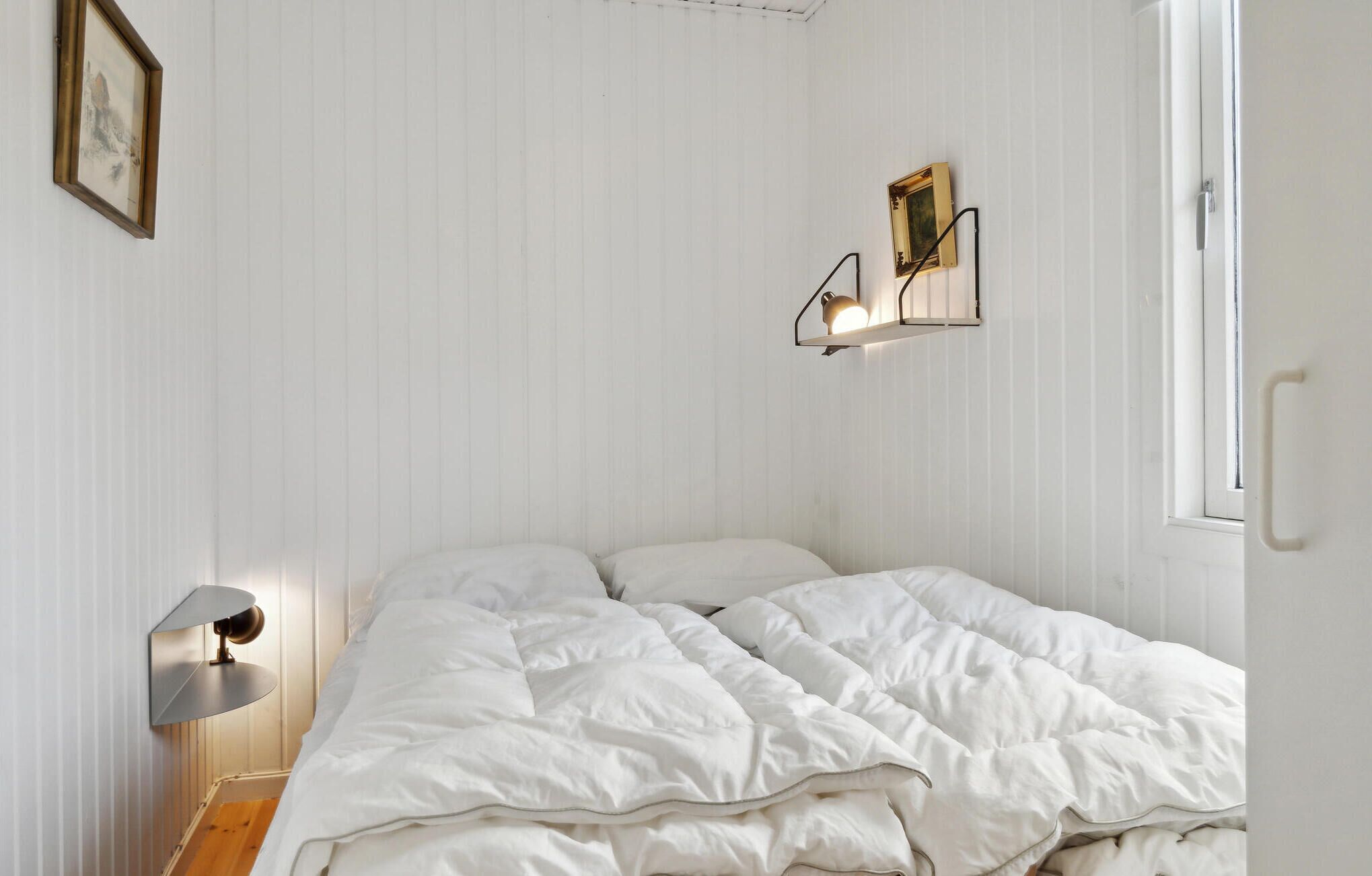 Ein Schlafzimmer mit einem Bett, einer Nachttischlampe, einer Wandleuchte und einem Fenster.