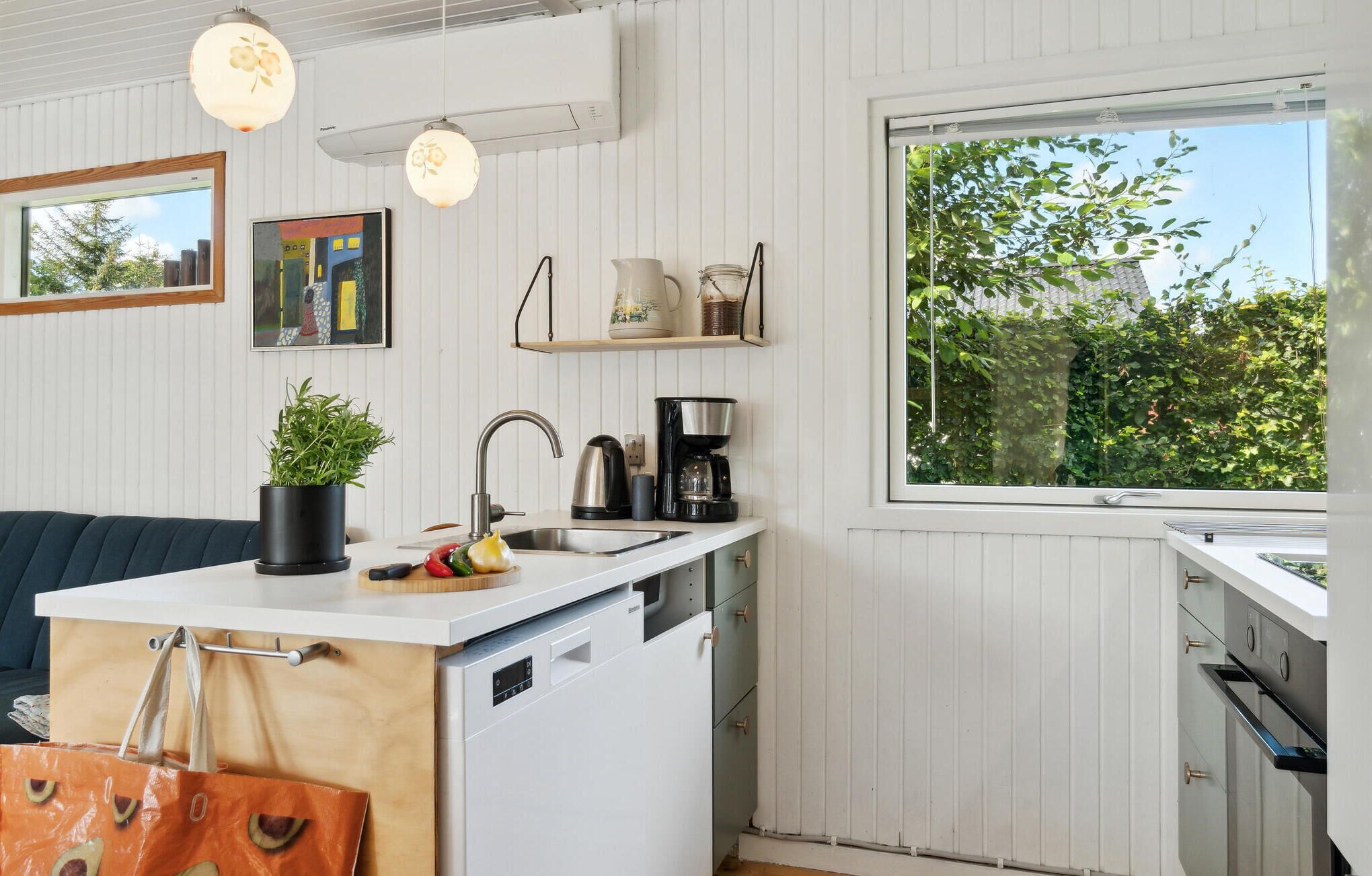 Una cucina moderna con mobili bianchi, lavastoviglie integrata, macchina del caffè e una pianta in vaso.