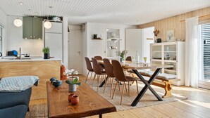 A modern kitchen with white cabinetry, a wooden dining table, and a cozy seating area with a sofa and chairs. - 5 bedroom nice home in Hadsund (Hadsund)